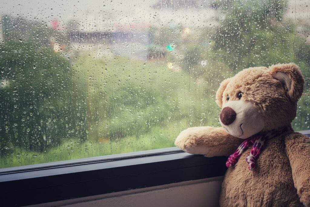 雨の窓の外を見る孤独なテディベア