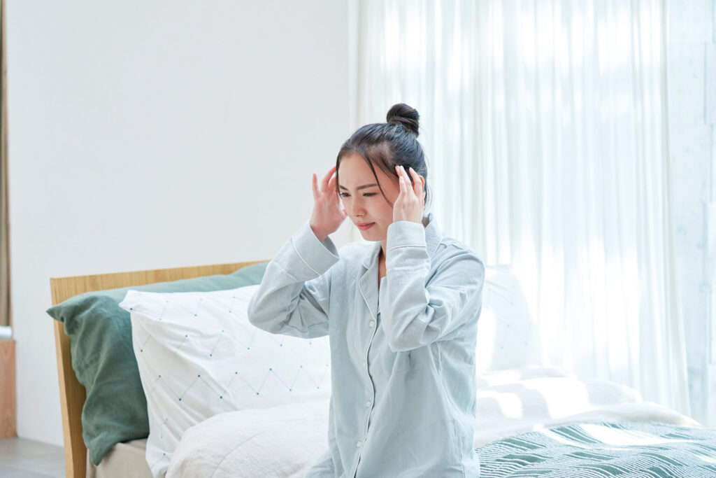 朝起きてもだるさが取れず頭を抱える女性のイメージ