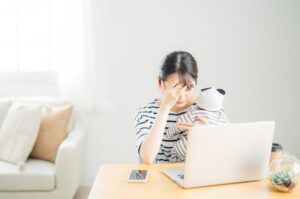 赤ちゃんを抱えながら仕事をこなし、体のだるさや頭痛に悩む産後の女性のイメージ
